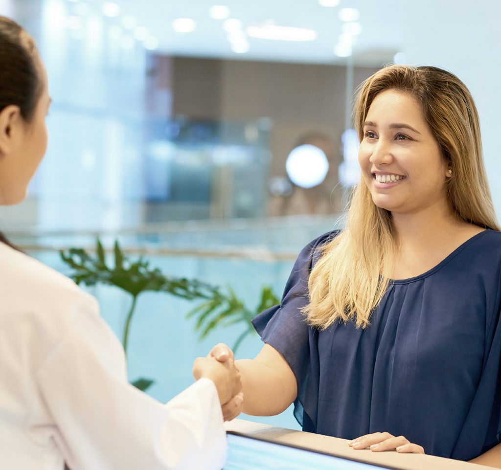 Smiling young woman shaking hand of doctor standing at reception